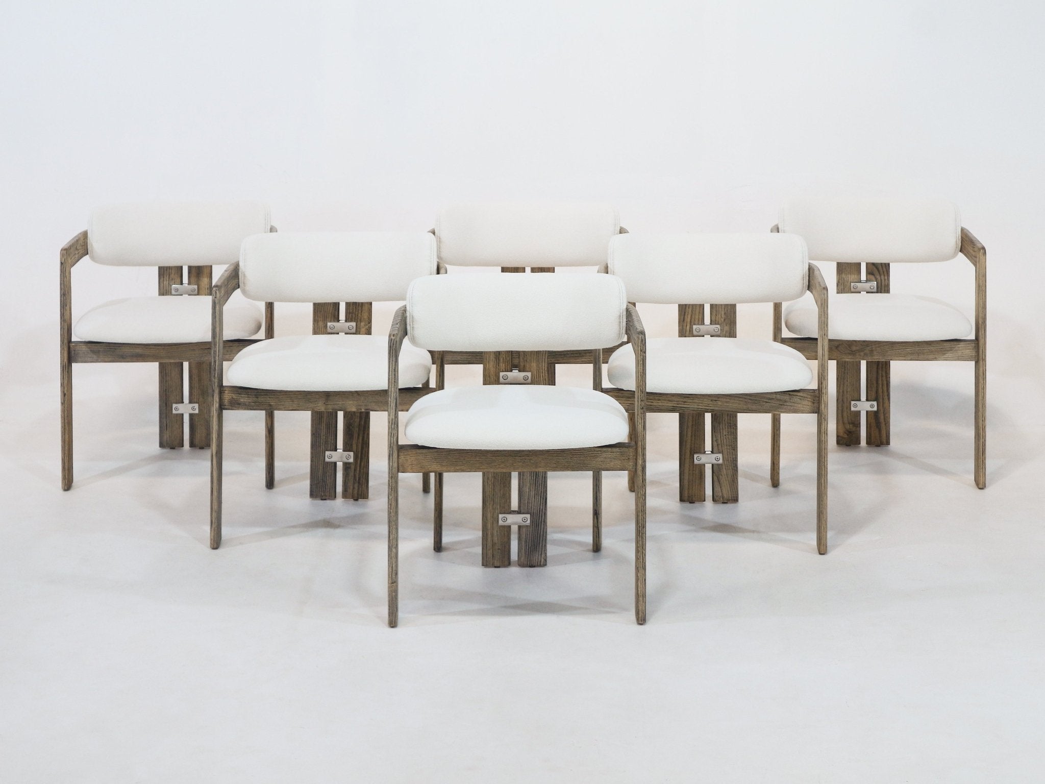 Studio image of a set of six rustic dining chairs with brown natural wood frames, cream-white boucle upholstered seats and curved backrests, metal bracket accents and slim armrests, arranged on a light seamless background.