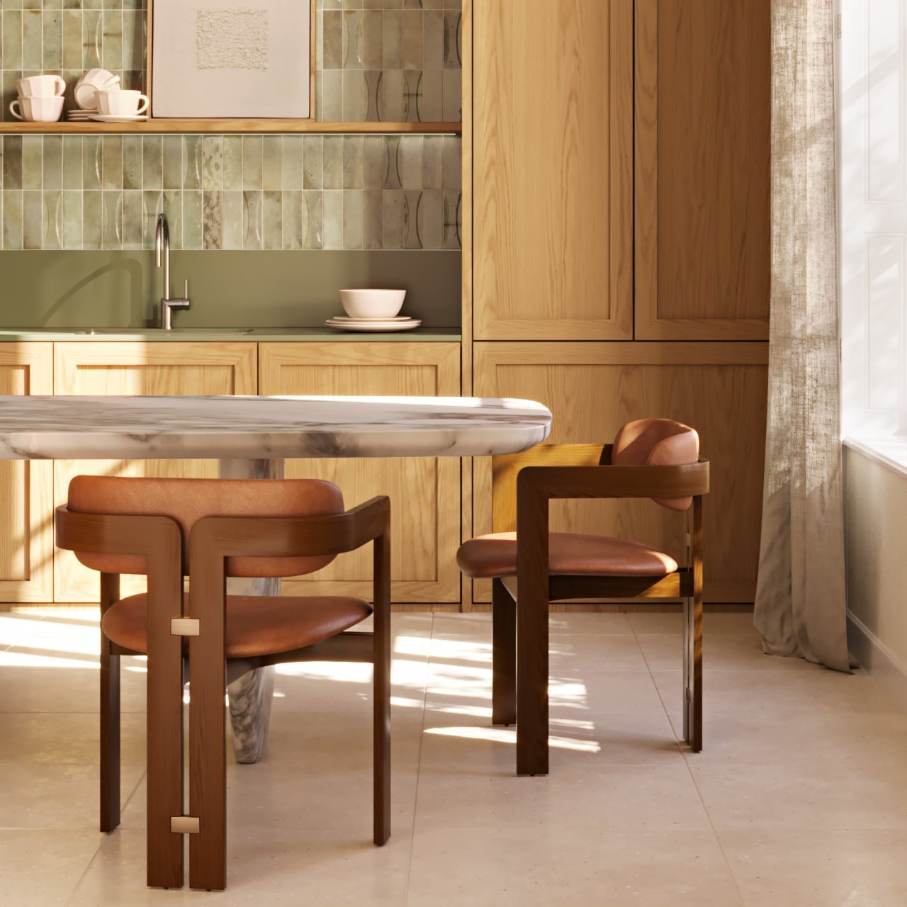 Two mid-century modern teak dining chairs with brown nubuck leather seats and brass square hardware beside a round marble table in a sunlit kitchen with natural wood cabinets and green tile backsplash.