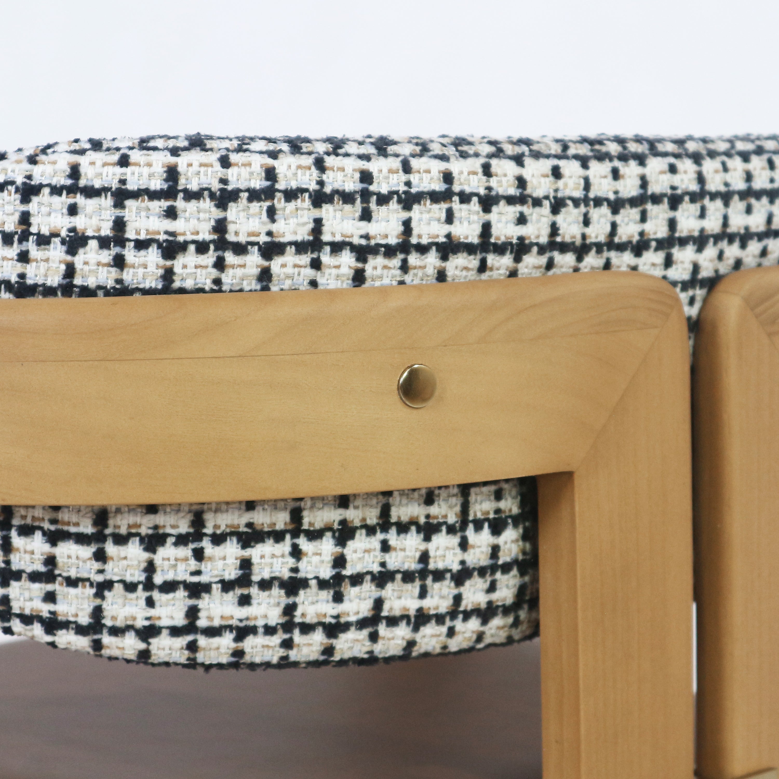 Close-up of a teak dining chair back showing the light teak wood frame, a round brass accent screw, and black-and-white textured woven fabric upholstery.