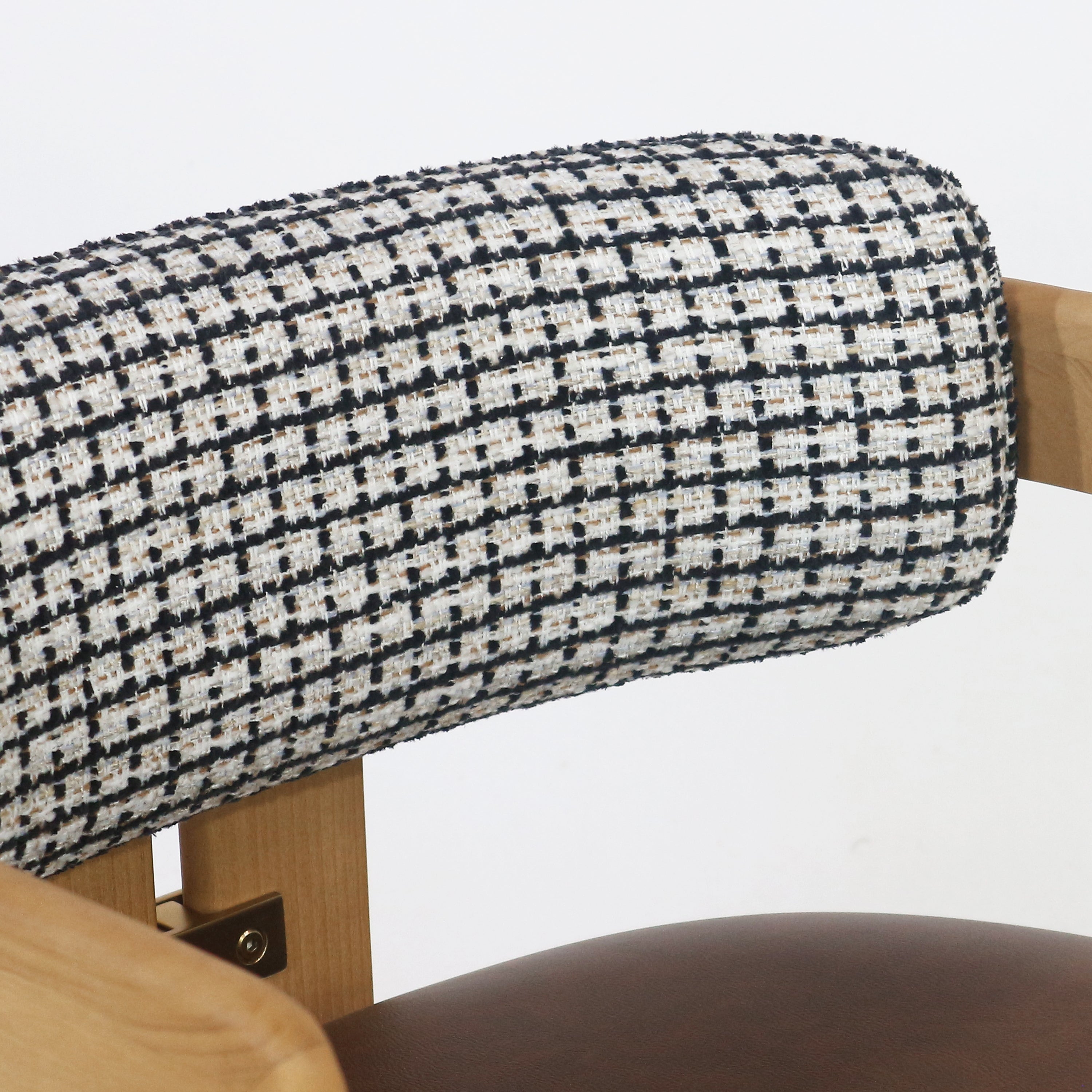 Close-up of a cylindrical black-and-white tweed-upholstered backrest on a teak dining chair showing the teak wood frame, visible brass bracket and a glimpse of the brown leather seat.