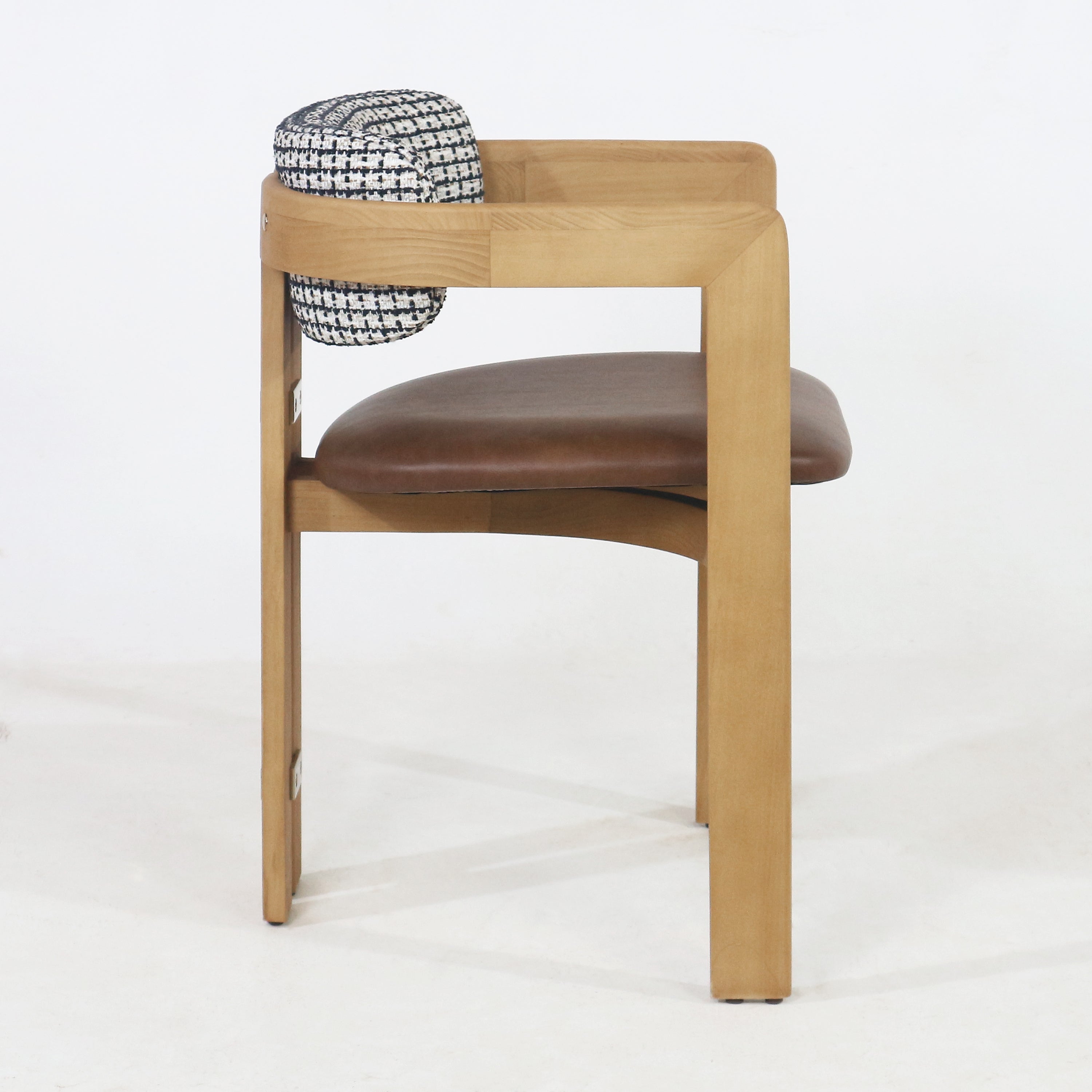 Side view of a mid-century modern dining chair with a light teak wood frame, curved arm, brown leather-upholstered seat and a black-and-white tweed fabric back cushion.