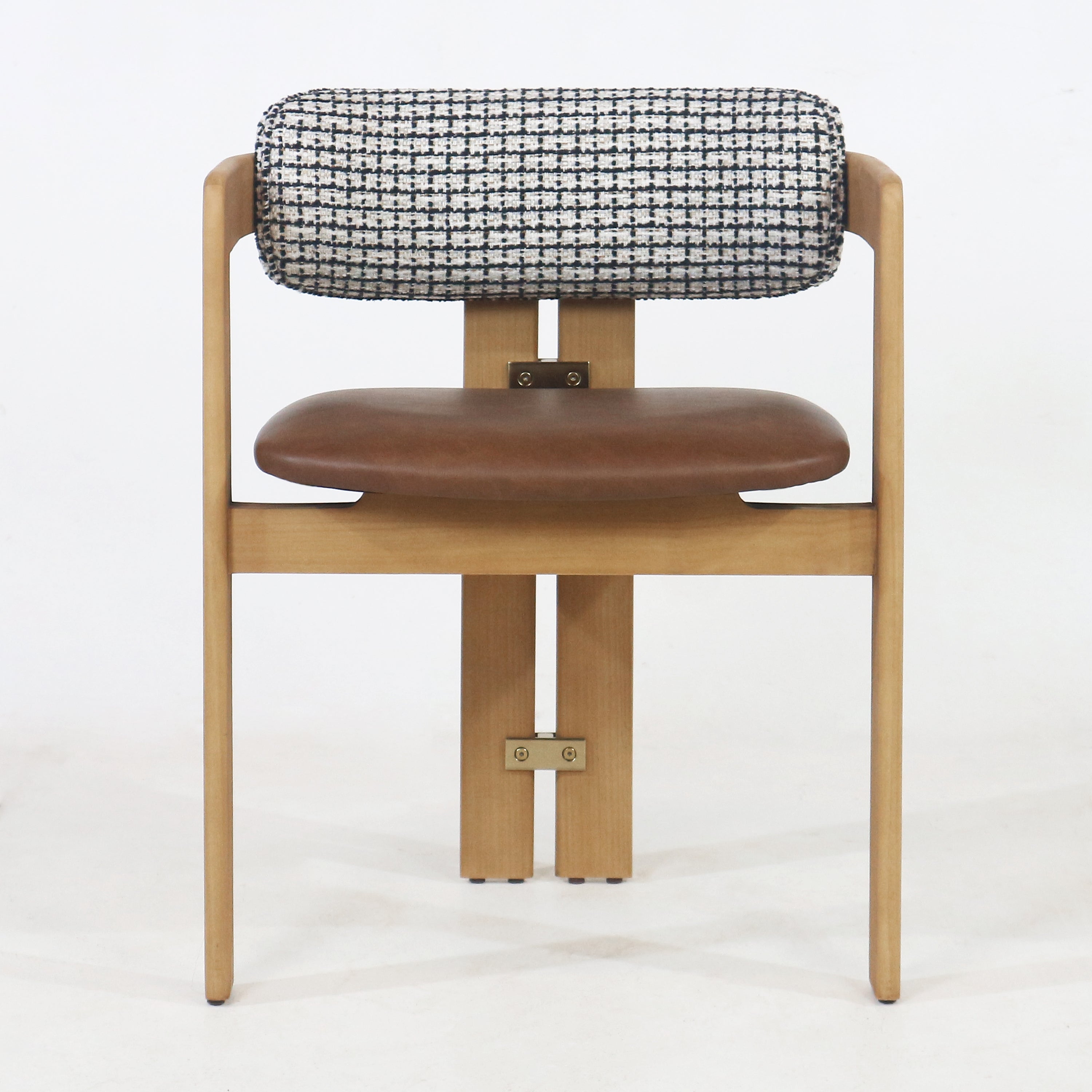 Front view of a mid-century modern teak dining chair with a light teak frame, black-and-white patterned tubular fabric backrest, brown leather-upholstered seat and visible brass bracket hardware.