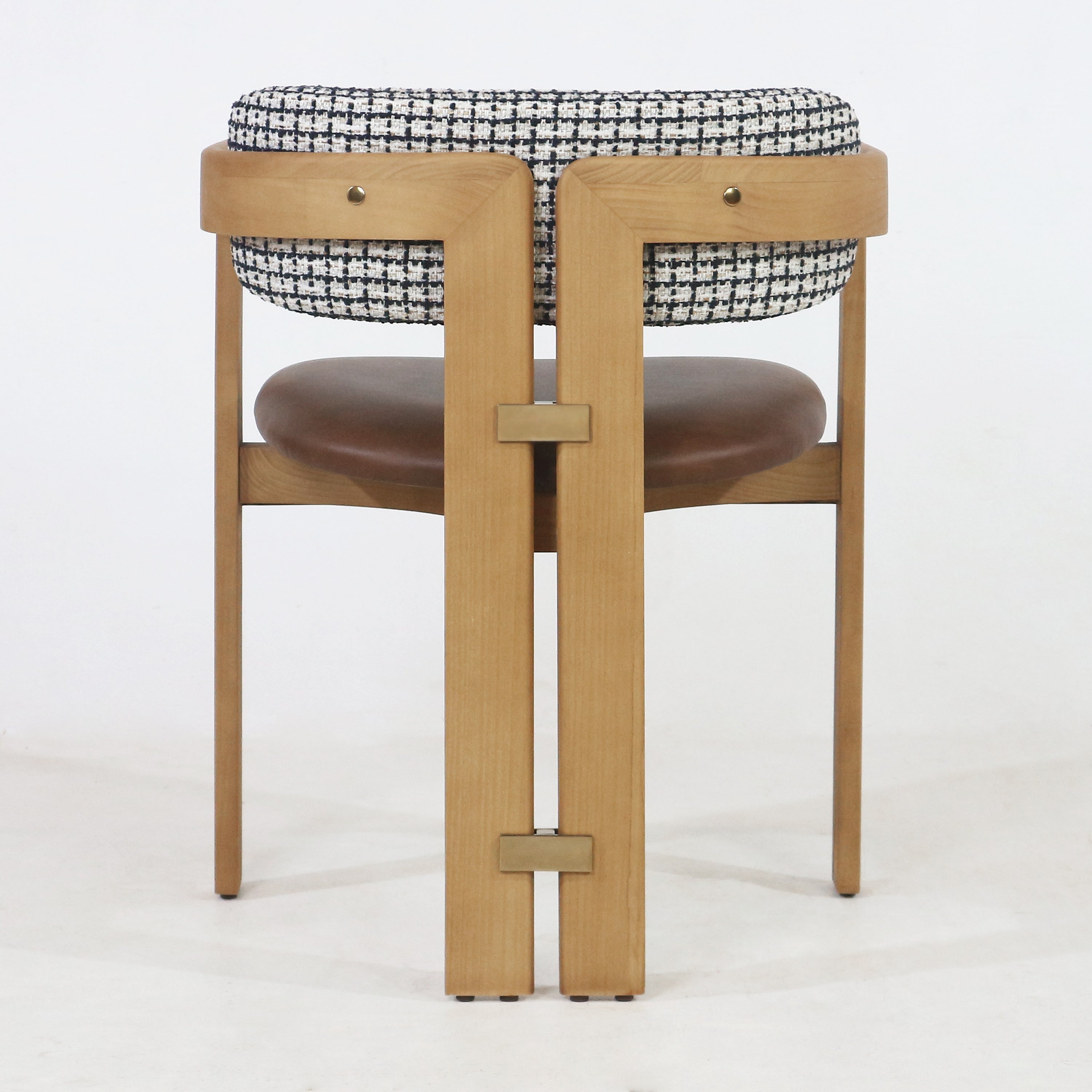 Rear view of a mid-century modern teak dining chair with black-and-white tweed fabric backrest, brown leather seat, brass hardware accents and slender teak legs.