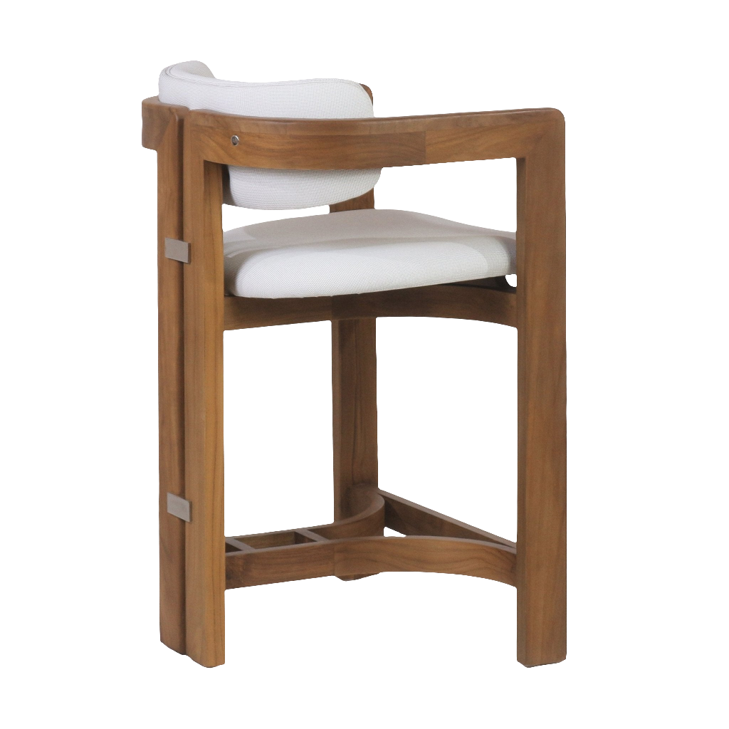 Side view of a teak outdoor bar stool showing a warm teak frame with squared legs and triangular stretcher footrest, a white upholstered seat and curved back cushion, and small stainless-steel hardware accents.