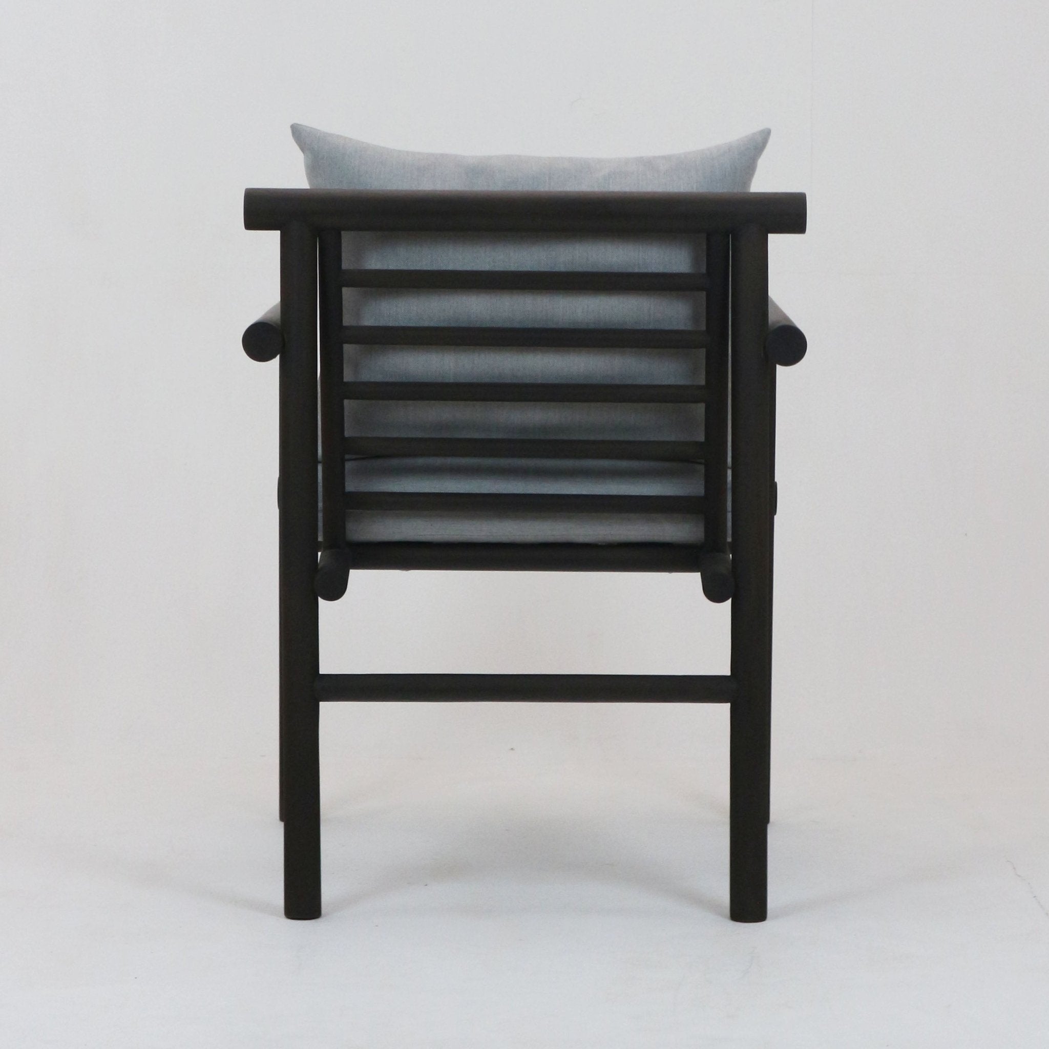 Rear view of a black teak patio chair with horizontal slatted back, rounded rail arms and a light gray Sunbrella fabric cushion pillow.