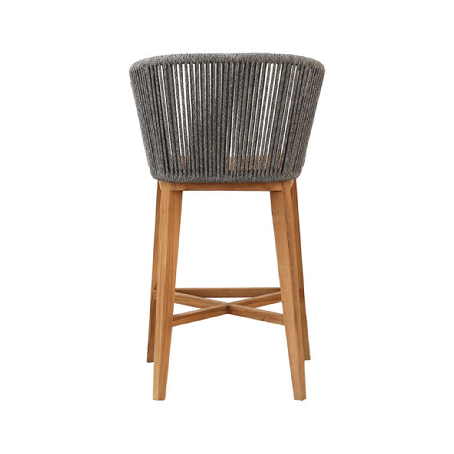 Rear view of a natural teak outdoor bar stool featuring a grey rope-wrapped barrel back and crossed teak stretchers connecting the tapered legs.