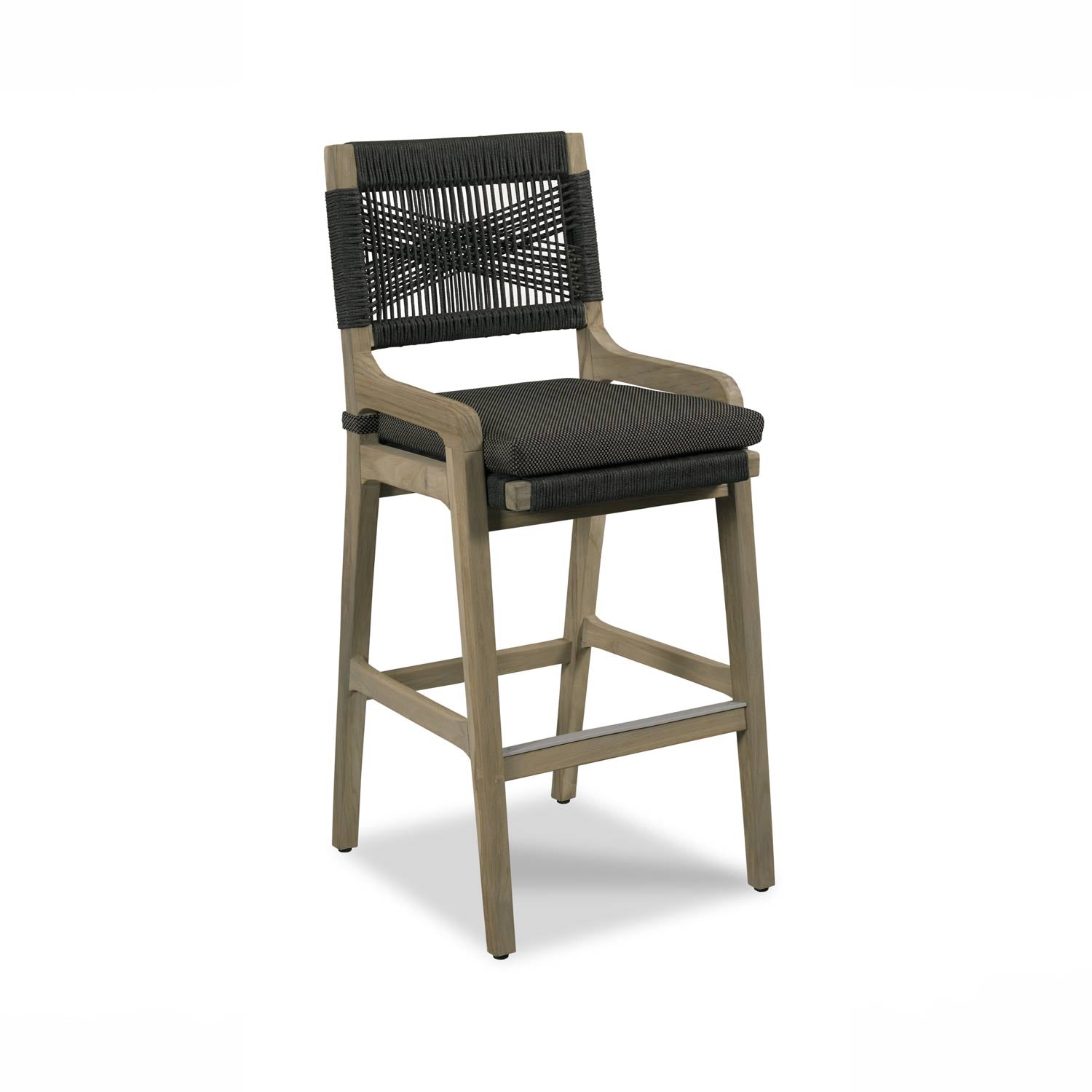 Natural teak outdoor bar stool with a woven black rope back, curved wooden armrests and a black textured fabric seat cushion on a solid teak frame with a metal footrest.