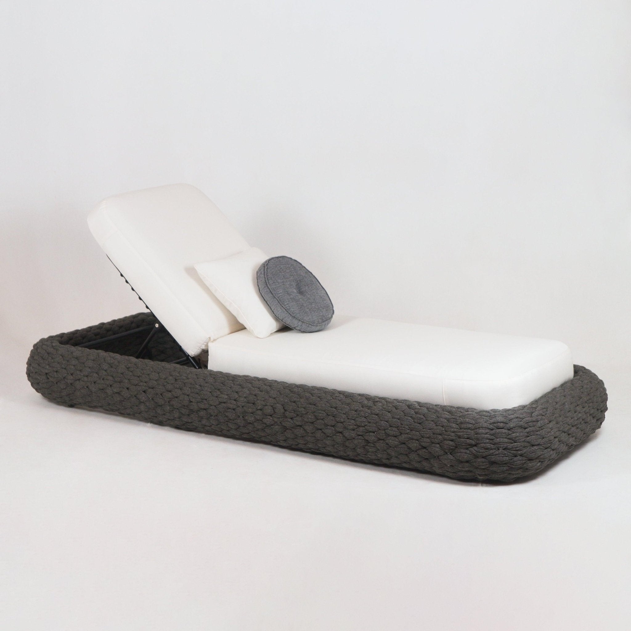 Outdoor coastal chaise lounger with a thick taupe rope-woven base, white fabric cushioned mattress and adjustable metal recline, shown with a rectangular white pillow and a round gray cushion.