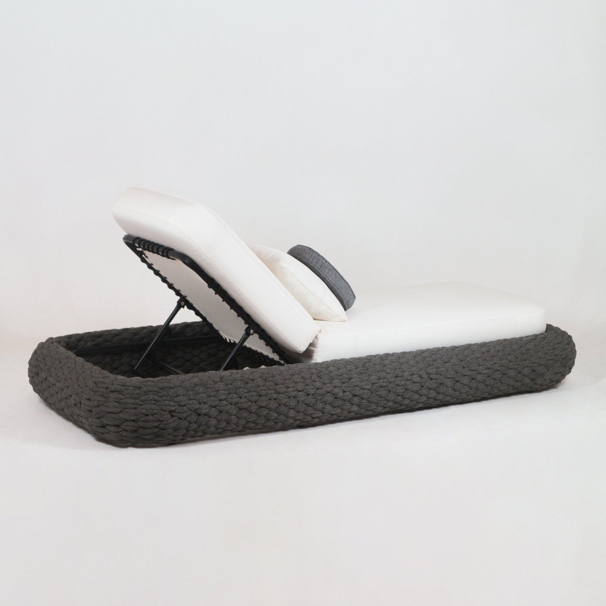 Outdoor poolside chaise with a taupe rope-woven base, white fabric cushions, an adjustable metal backrest and a gray bolster pillow, displayed on a neutral background.