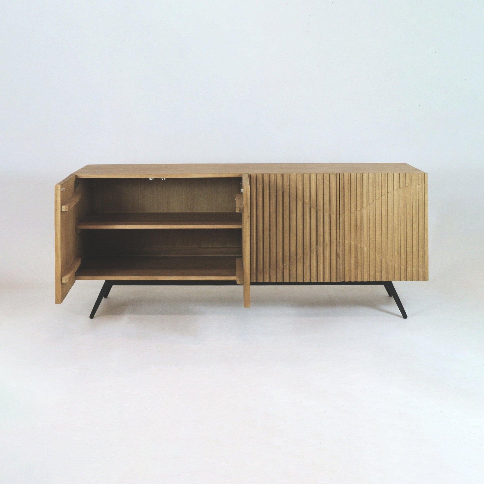 Mid-century modern teak sideboard with vertical ribbed front panels and black iron legs; left door open to show two interior shelves, photographed on a plain white studio background.