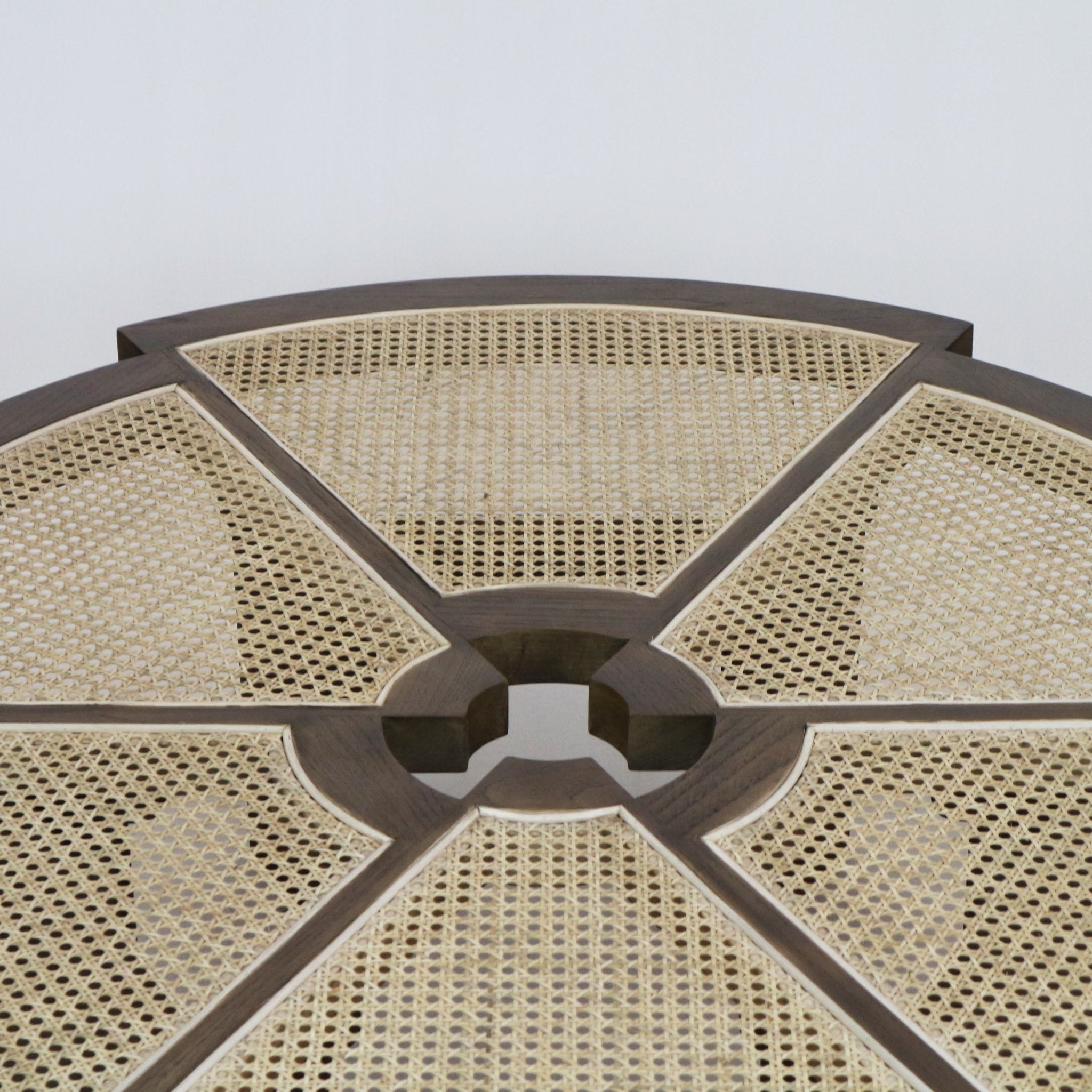 Close-up of a round coffee table top featuring natural cane-woven panels set into a teak-brown solid wood frame divided into radial sections with a circular center opening.
