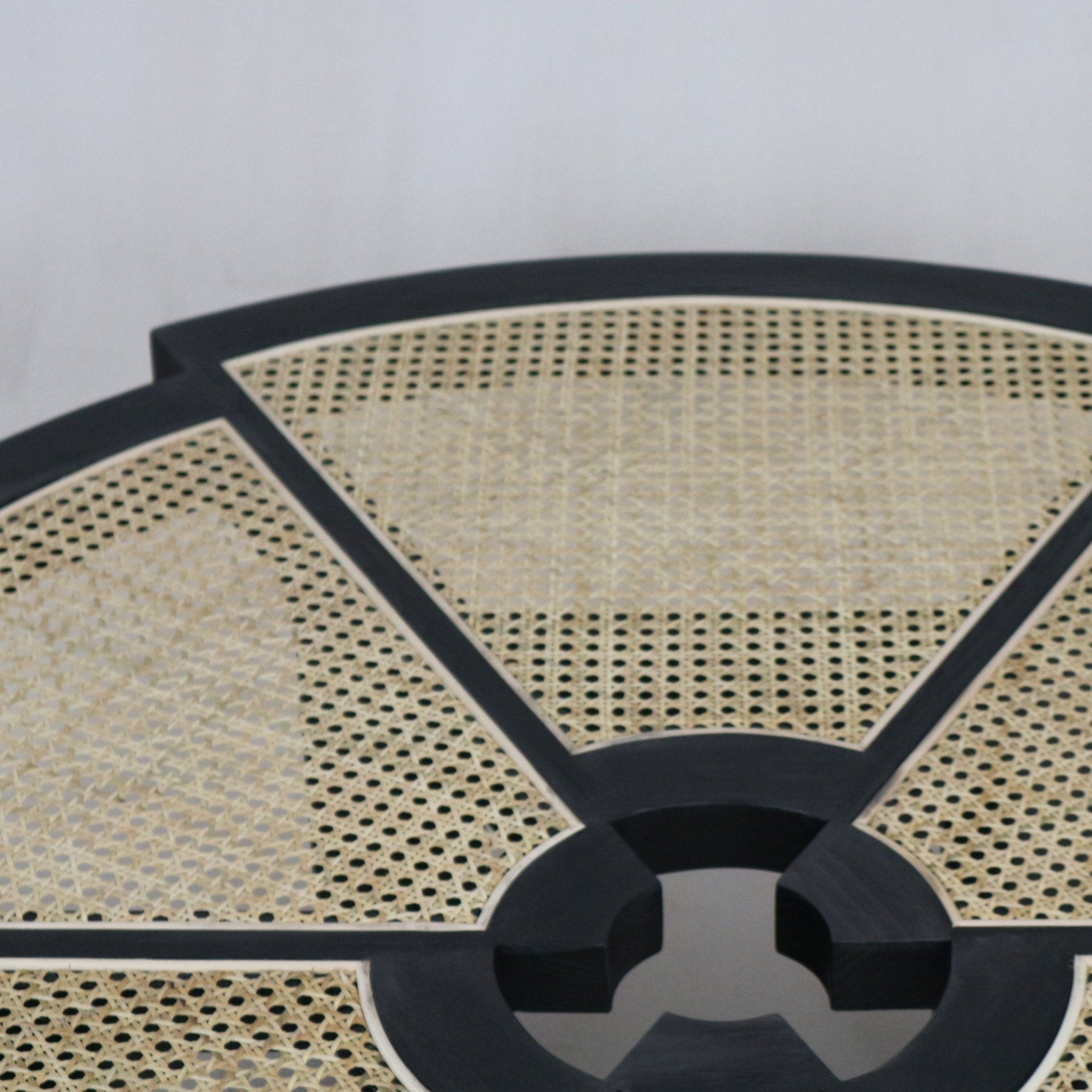 Close-up of a round coffee table top showing natural cane weave panels set into a smoked-black solid wood frame with radial spokes and a central circular cutout, highlighting the piece’s modern mid-century inspired detailing.