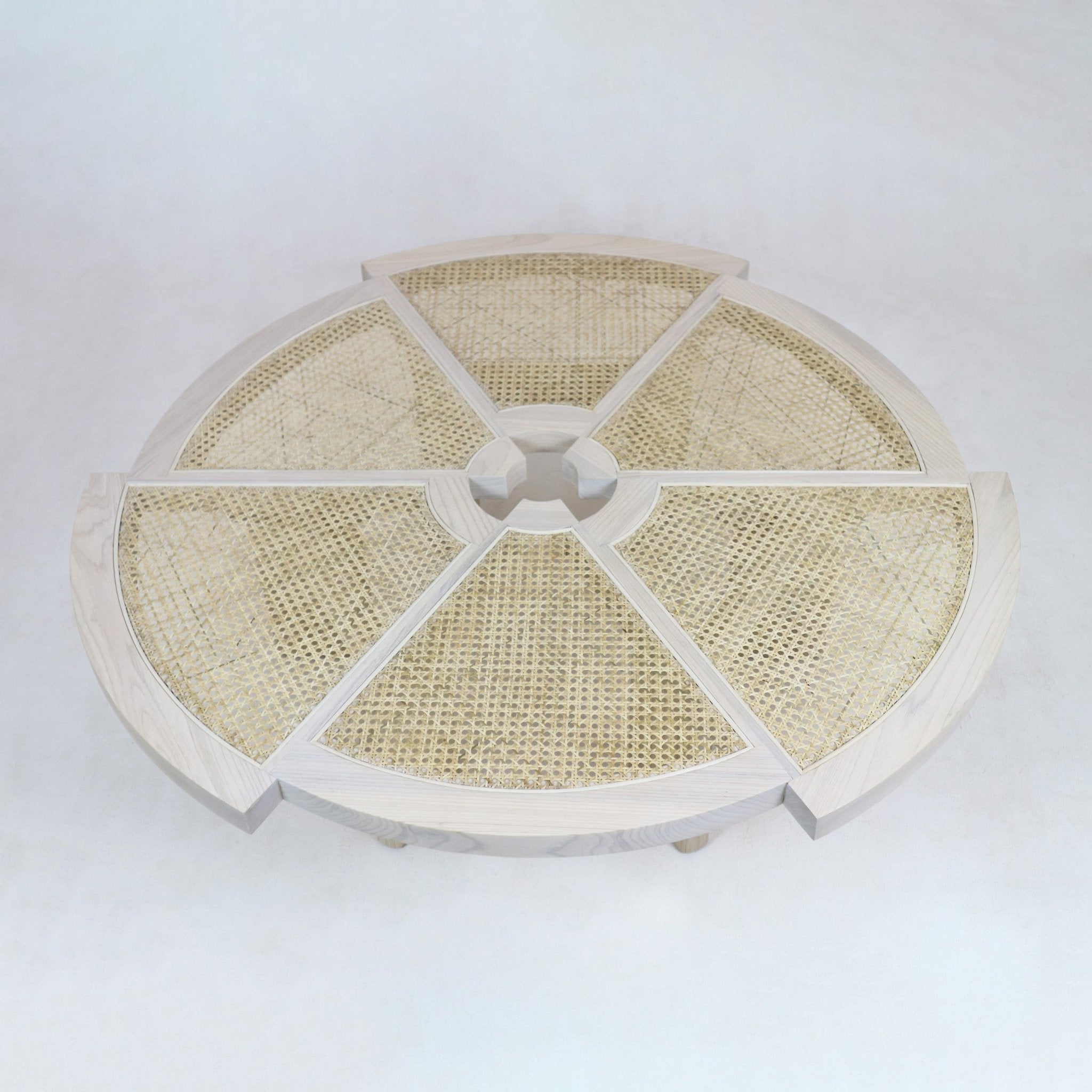 Top-down view of a round natural wood coffee table with six cane-woven inlay panels radiating from a central circular hub, finished in a light blonde tone for a modern contemporary living room.