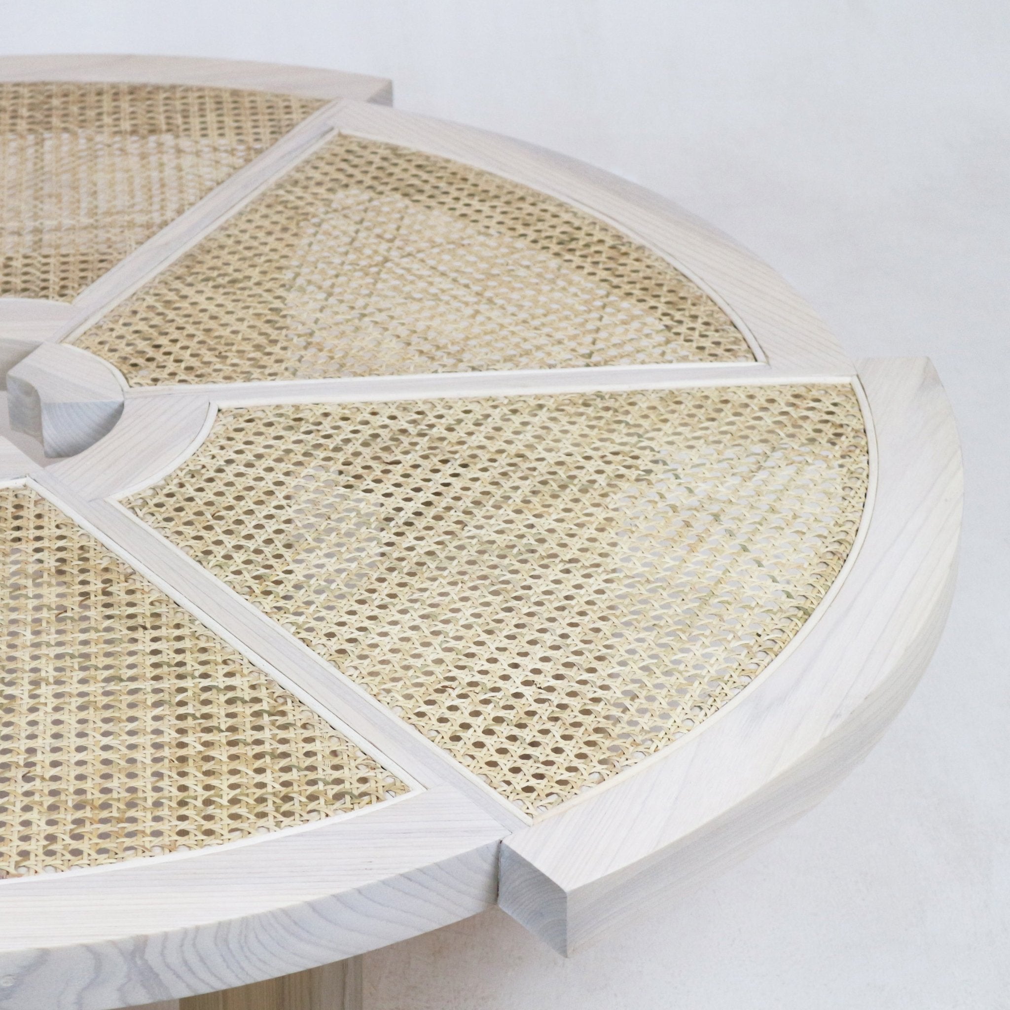 Close-up of a round coffee table top with a light natural wood frame, four radial dividers and woven cane panels in a neutral beige tone.