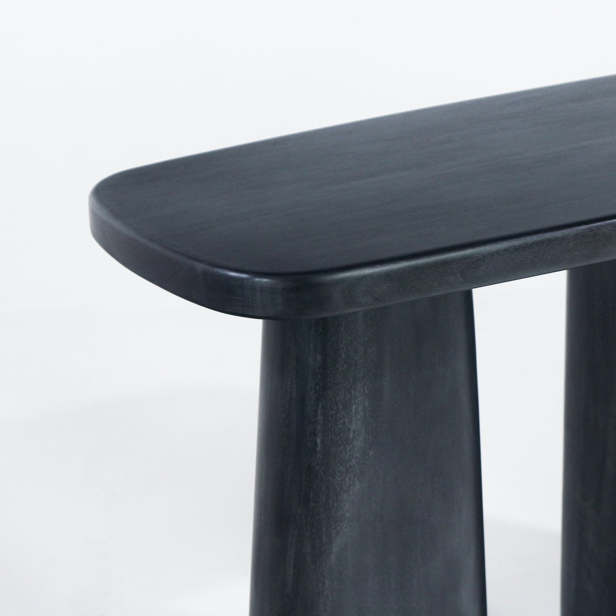 Close-up of a black solid wood console table corner showing the smooth rounded tabletop edge and tapered cylindrical legs in a modern finish.