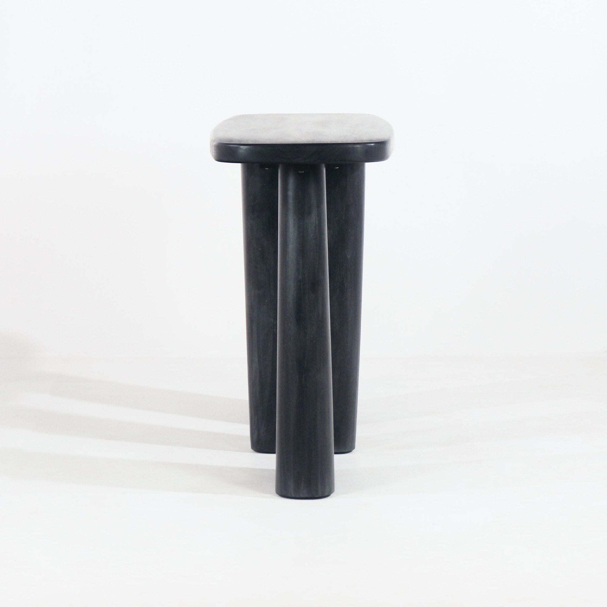 Front view of a smoked-black solid wood console with a rounded rectangular top and three thick cylindrical tapered legs on a white studio background.