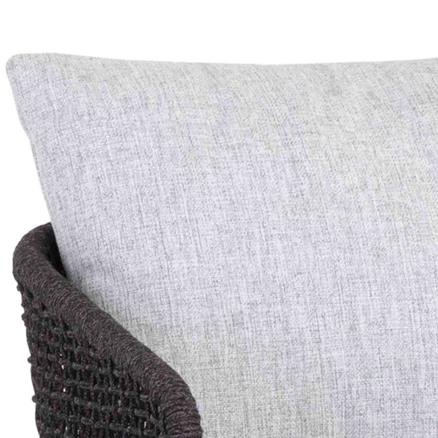 Close-up of a light gray upholstered fabric back cushion leaning against a dark woven rope arm, shown as part of a teak outdoor bar stool in a neutral coastal style.