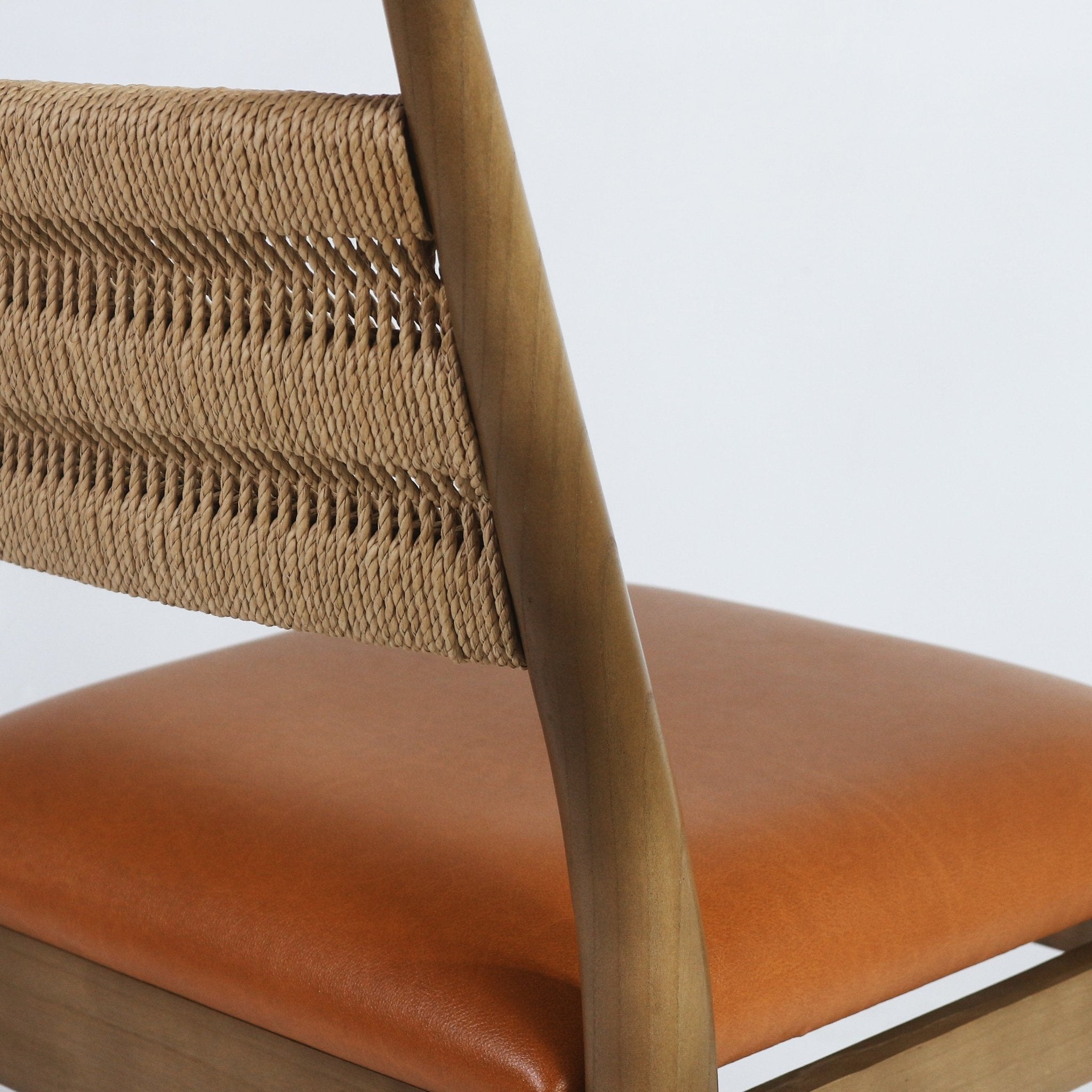 Close-up of a side chair showing a woven natural rope back, curved light-wood frame and cognac faux leather upholstered seat.
