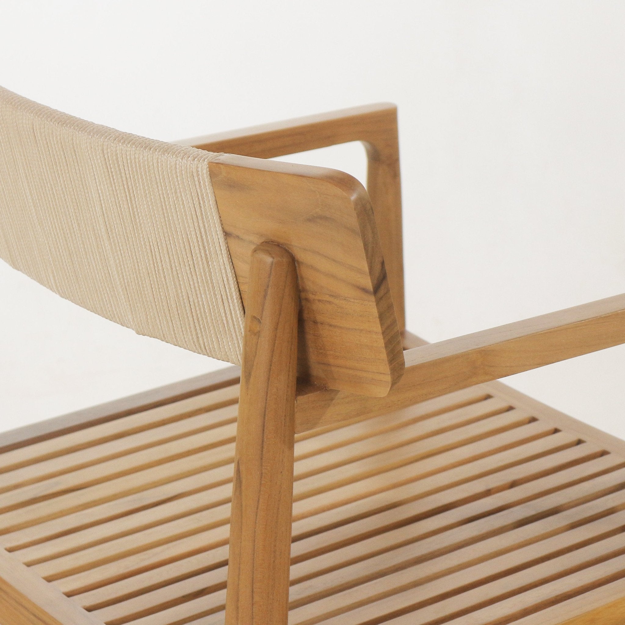 Close-up of a natural teak outdoor dining chair showing a beige woven backrest, rounded teak arm and leg joint, and the slatted teak seat detail.