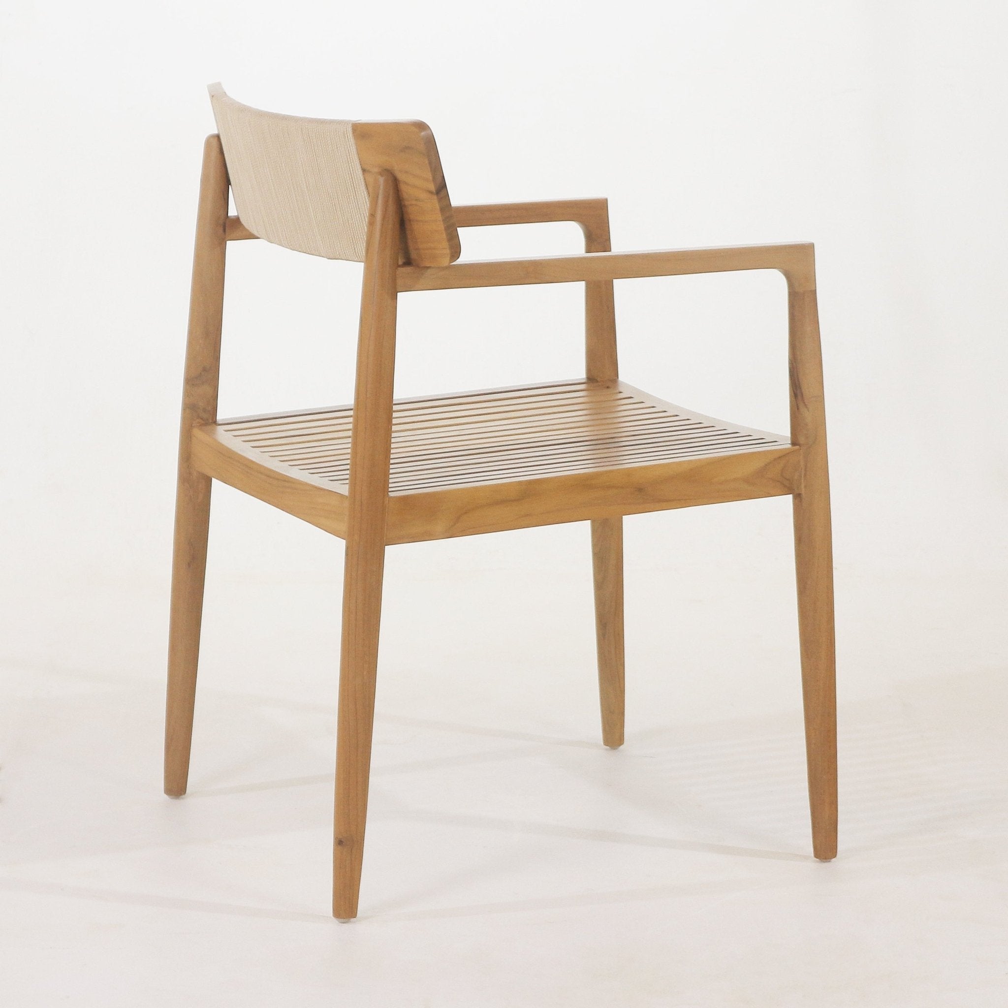 Side view of a natural teak outdoor dining chair with a slatted teak seat, tapered legs, squared armrests and a light woven beige back strap in a coastal mid-century modern style.