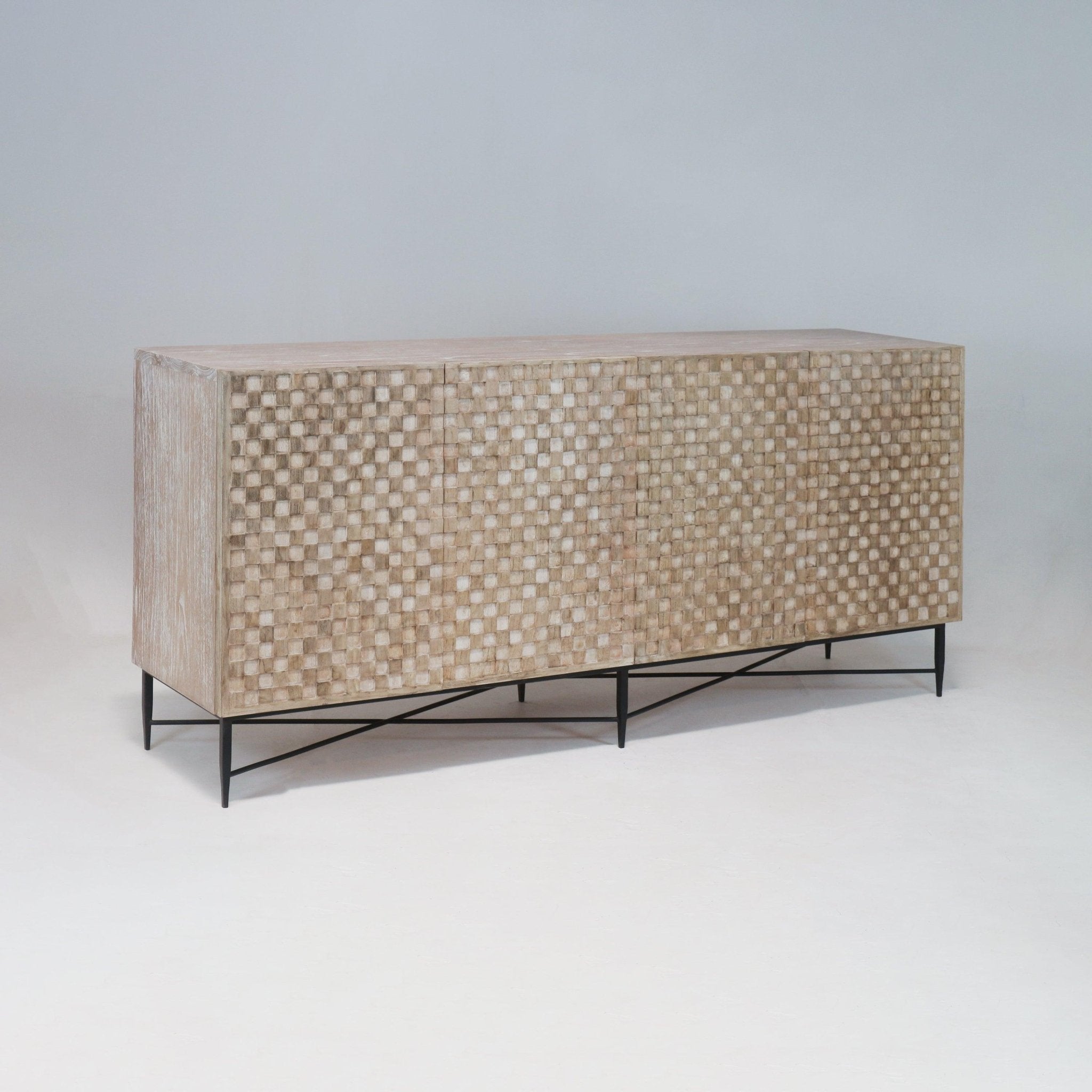 Long mid-century modern teak sideboard with a whitewashed natural finish, textured checkerboard carved front doors and a slim black metal base with crossed supports, photographed on a neutral studio background.