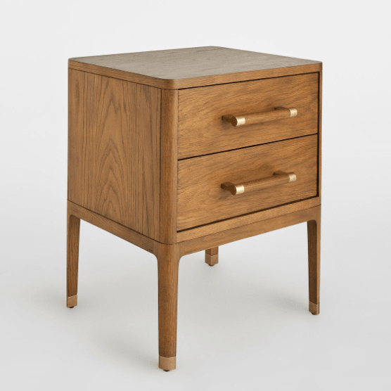 Warm brown solid wood nightstand with two drawers, rounded corners and slim tapered legs; brass bar handles and brass-capped feet add a glam-contemporary accent.