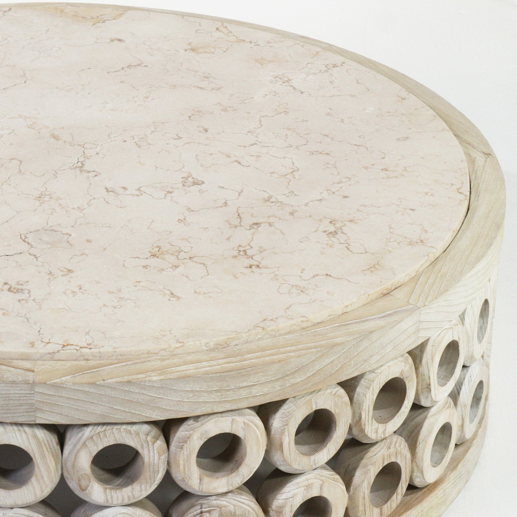 Close-up of a round coffee table showing a creamy travertine tabletop with subtle brown veining and a natural oak base composed of stacked carved circular hollow rings in a modern, contemporary style.