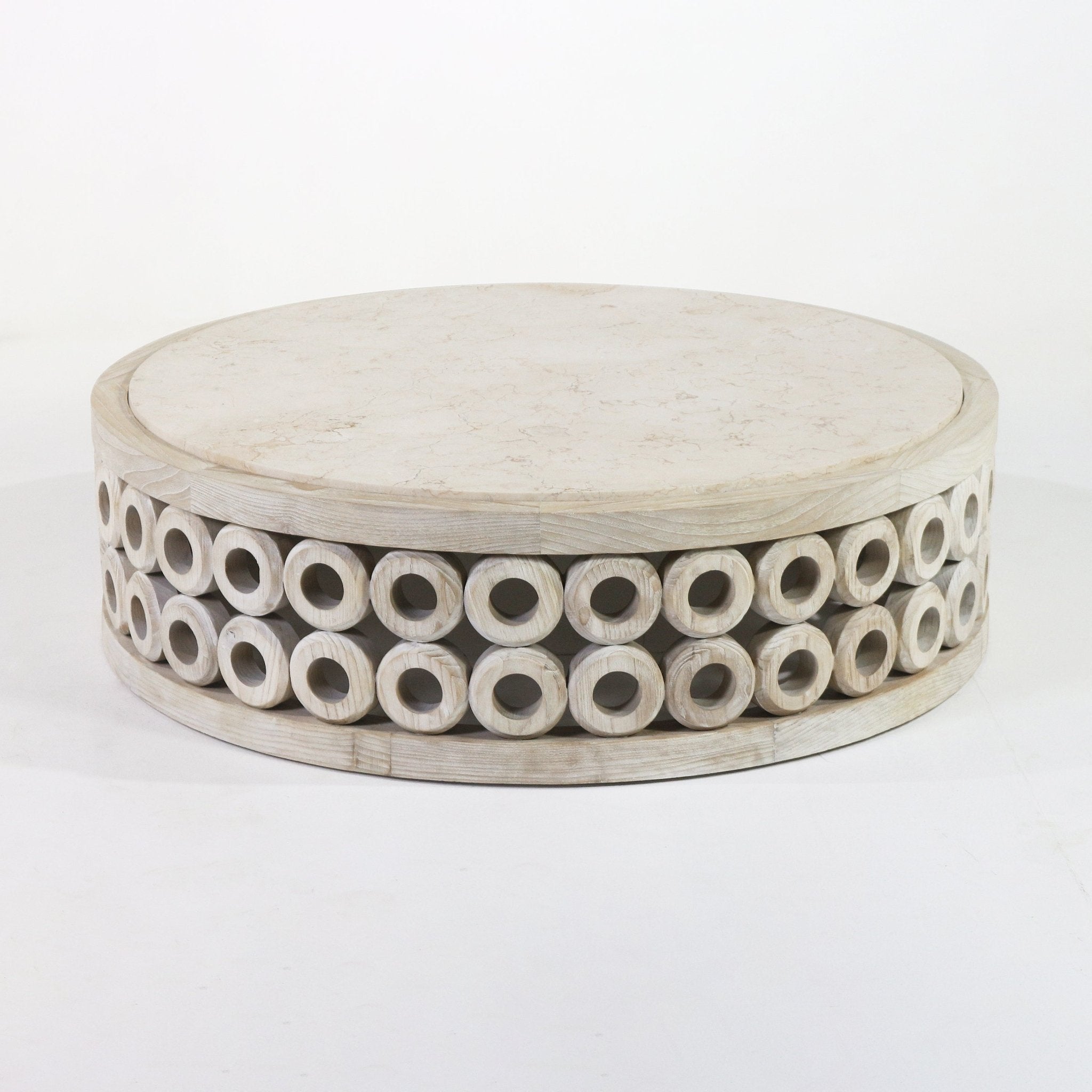 Low round coffee table with a light travertine stone top and a natural oak base composed of two stacked rows of carved hollow wooden rings.