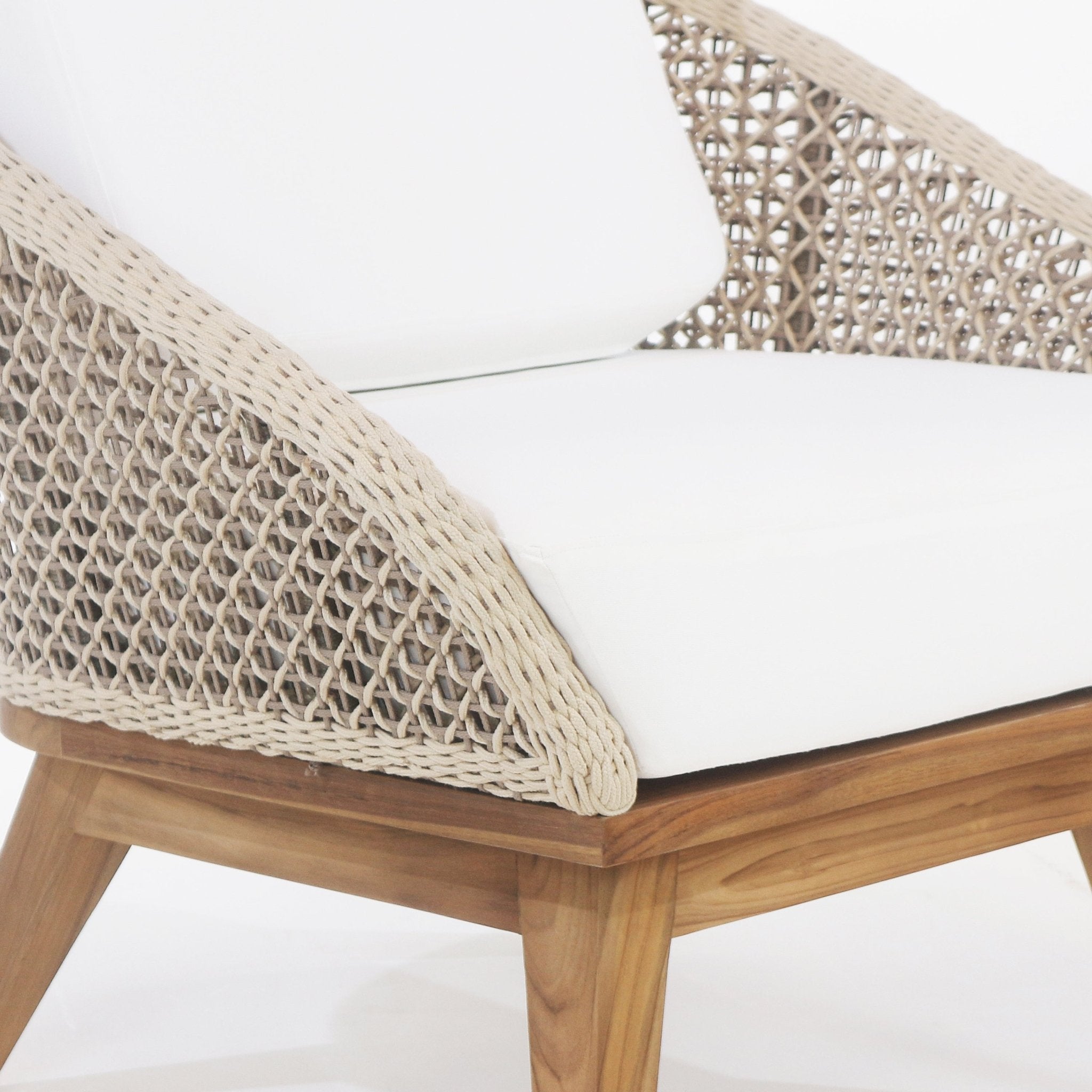 Close-up of an outdoor accent chair showing beige rope woven arm and back, white fabric seat and back cushions, and a natural teak wood frame with angled legs.