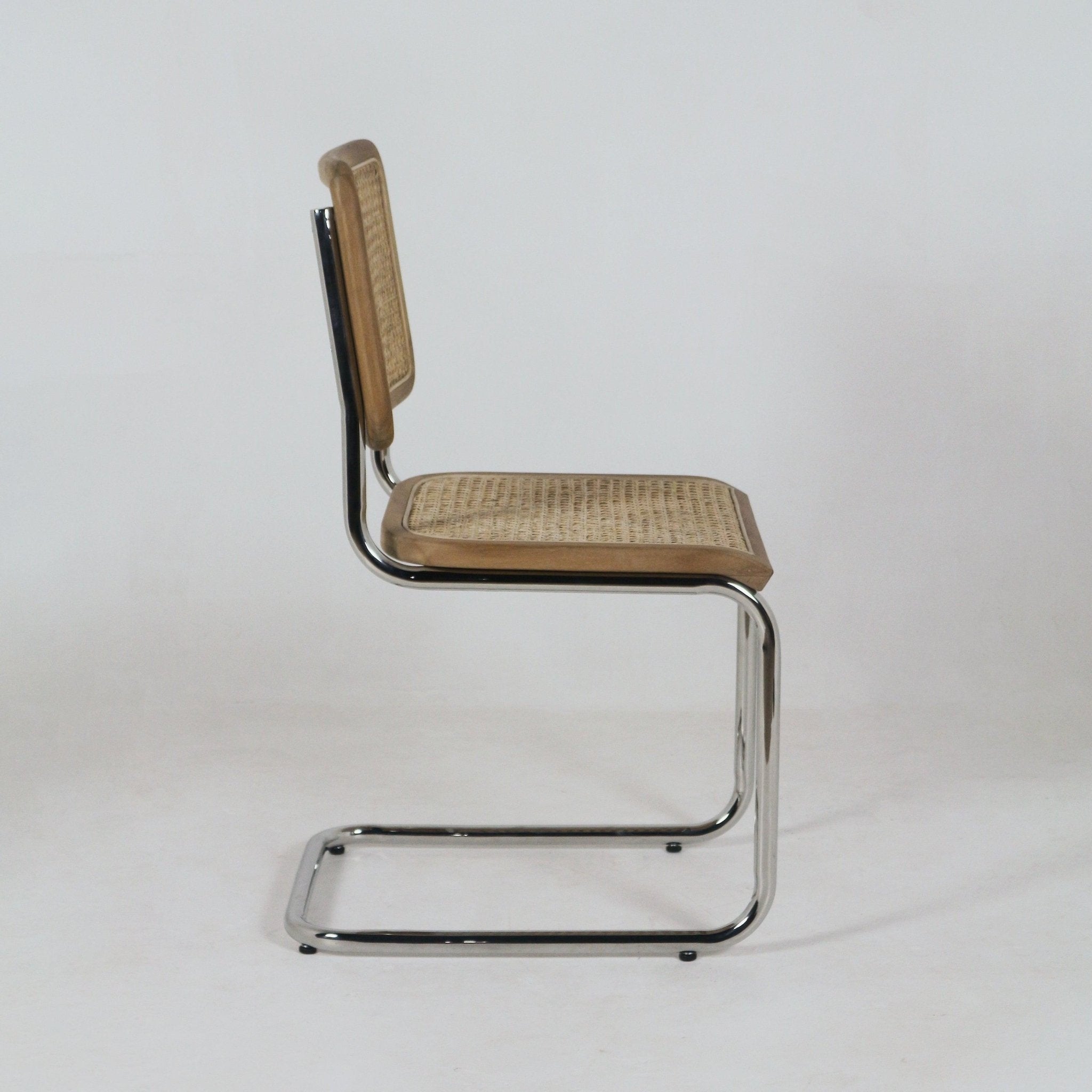 Side profile of an armless dining chair with teak wood edging and woven rattan seat and back mounted on a polished aluminium cantilever frame against a plain white background.