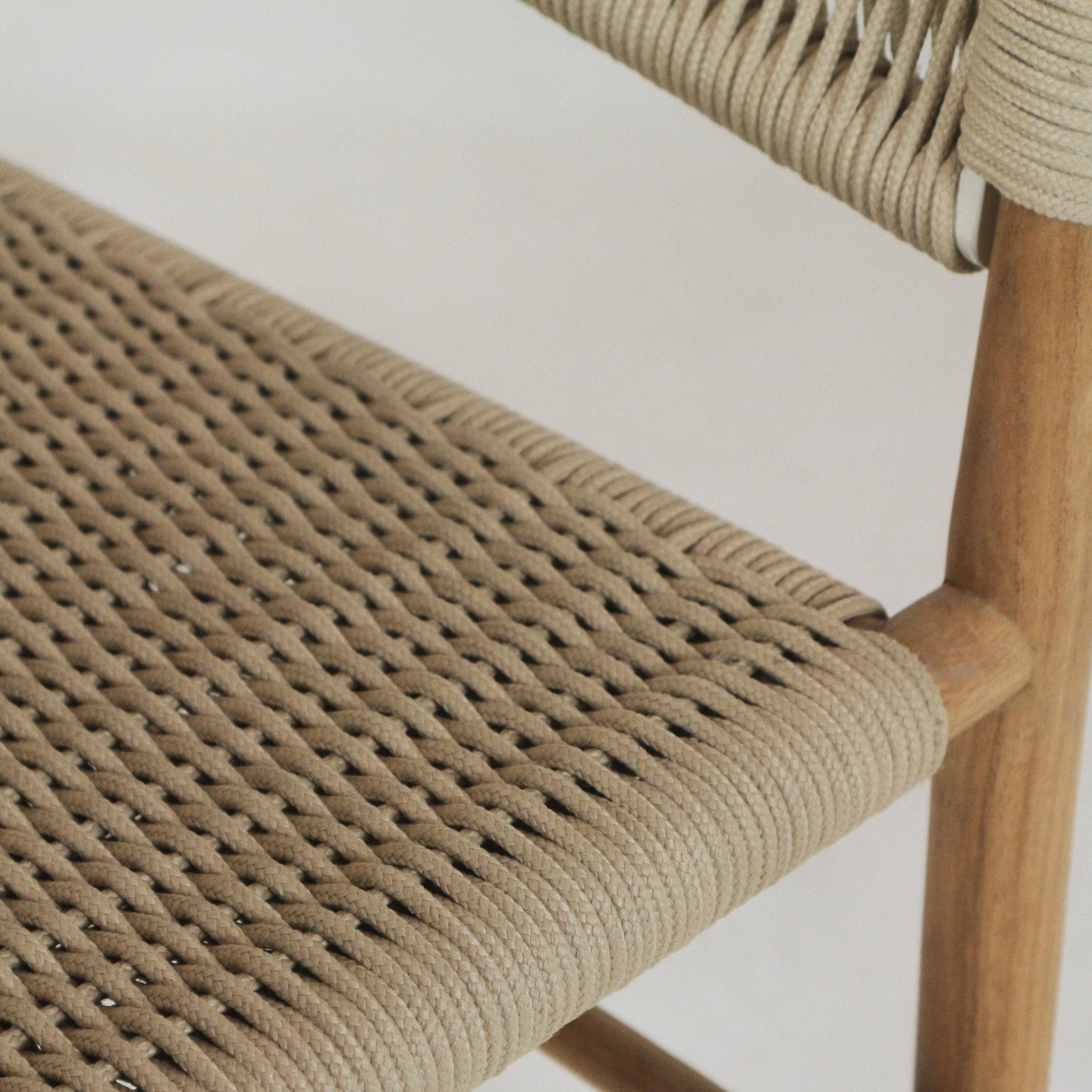 Close-up of a teak dining chair showing the beige polypropylene rope woven seat with a wrapped front edge and a natural teak wood leg.