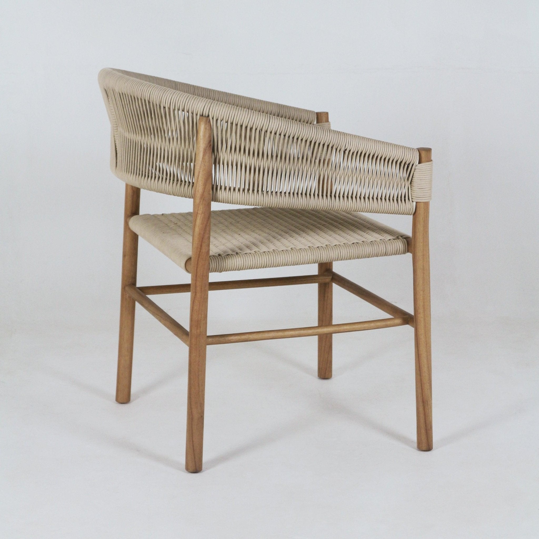 Rear three-quarter view of a teak dining chair with a light beige polypropylene woven back and seat, integrated low arms and curved backrest, supported by slender solid teak legs in a coastal contemporary style.