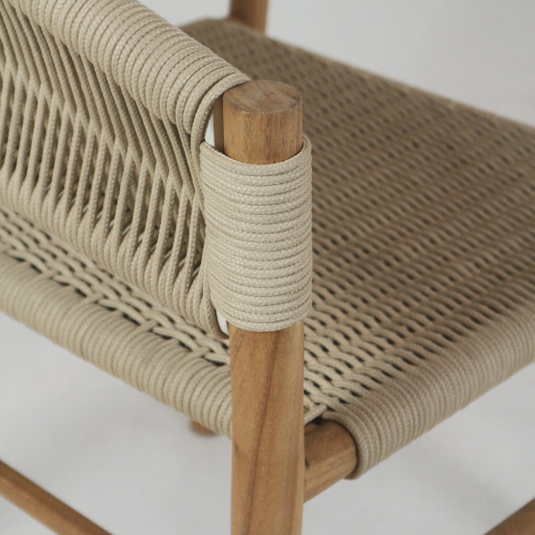 Close-up of a teak dining chair showing beige polypropylene rope woven seat and back tightly wrapped around the solid teak frame and arm post.