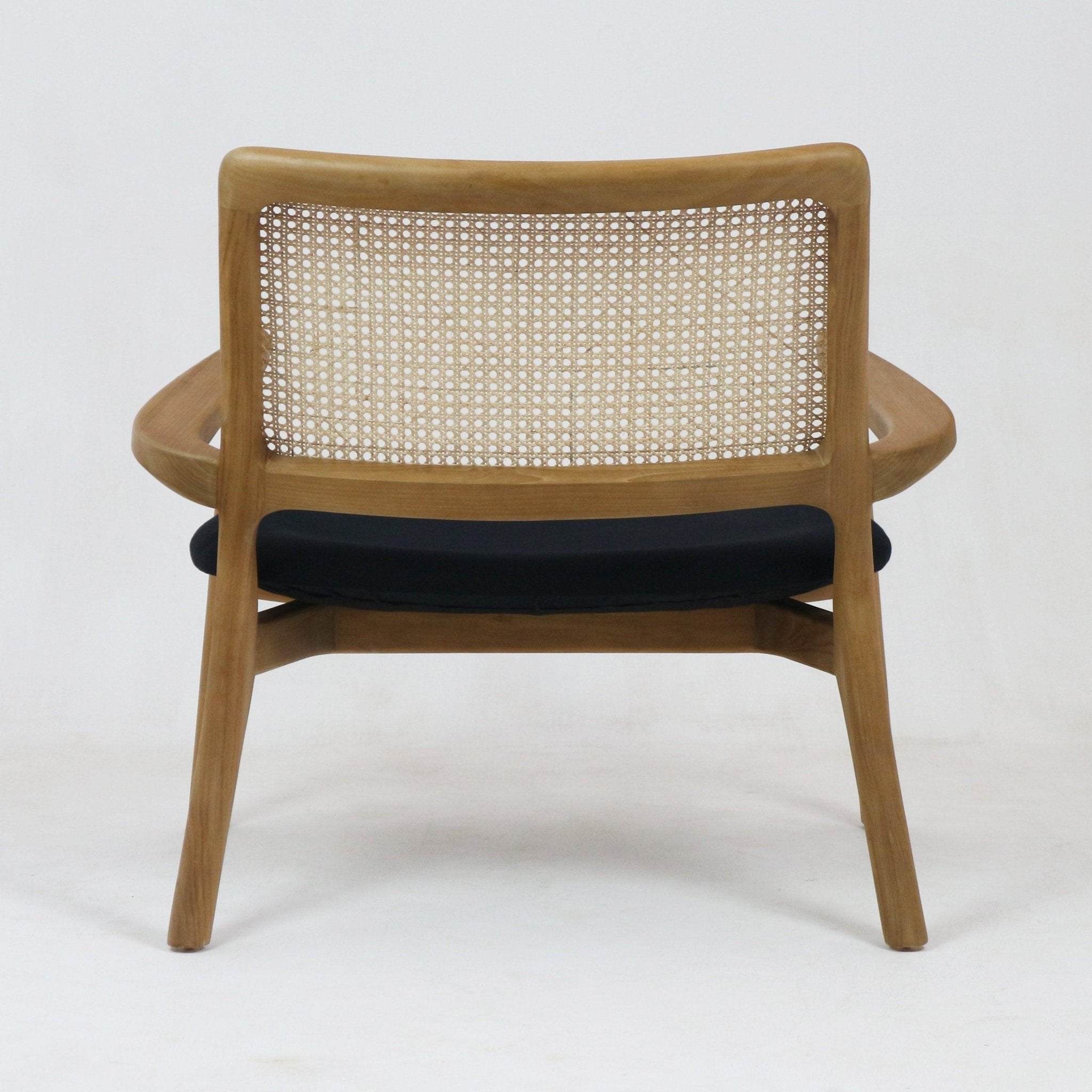 Rear view of a mid-century modern teak lounge chair with a woven cane backrest, curved solid teak frame and a black upholstered seat cushion.