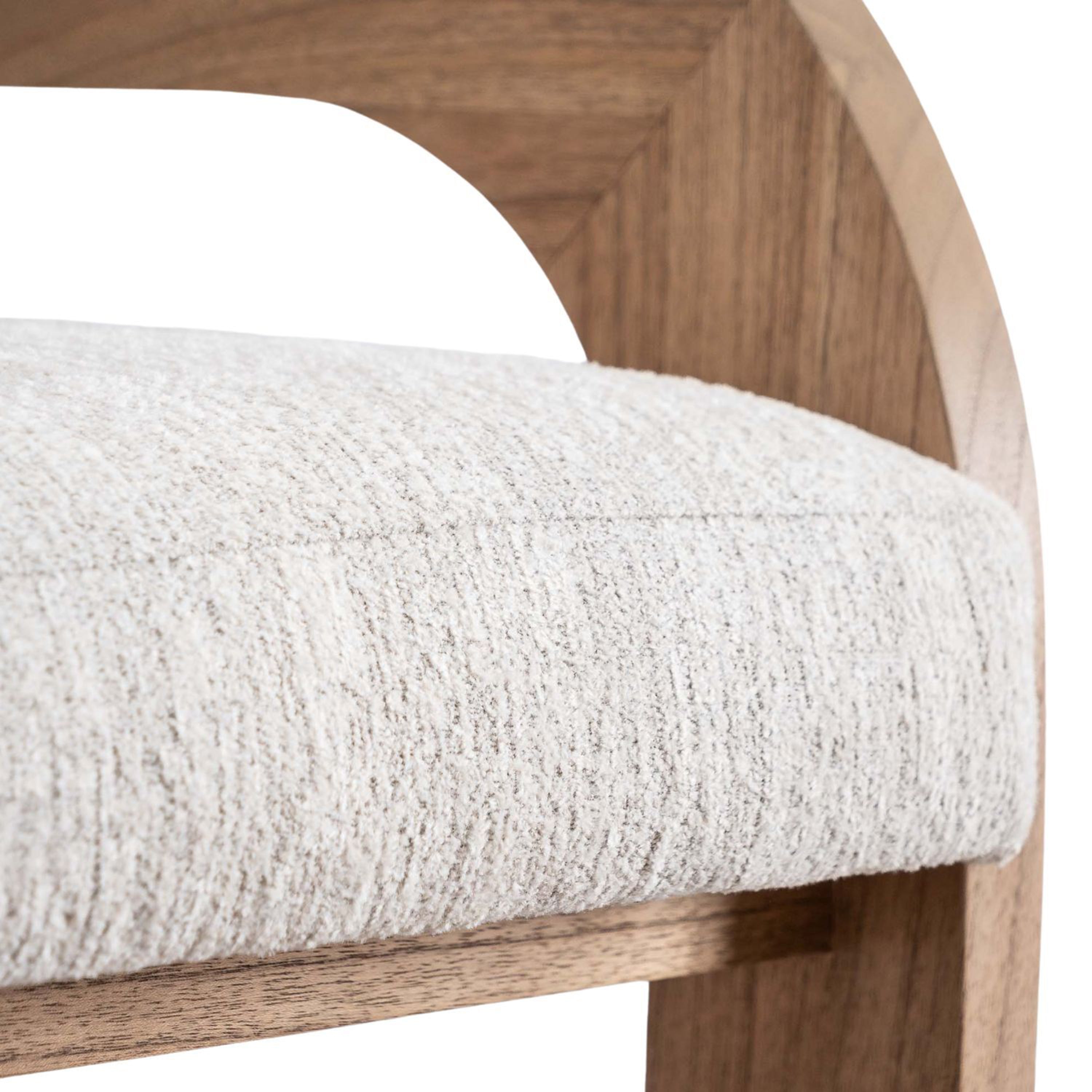 Close-up of a cream textured fabric seat cushion and the natural wood U-shaped back and armrest of a modern upholstered counter stool, highlighting the fabric texture and wood grain frame.