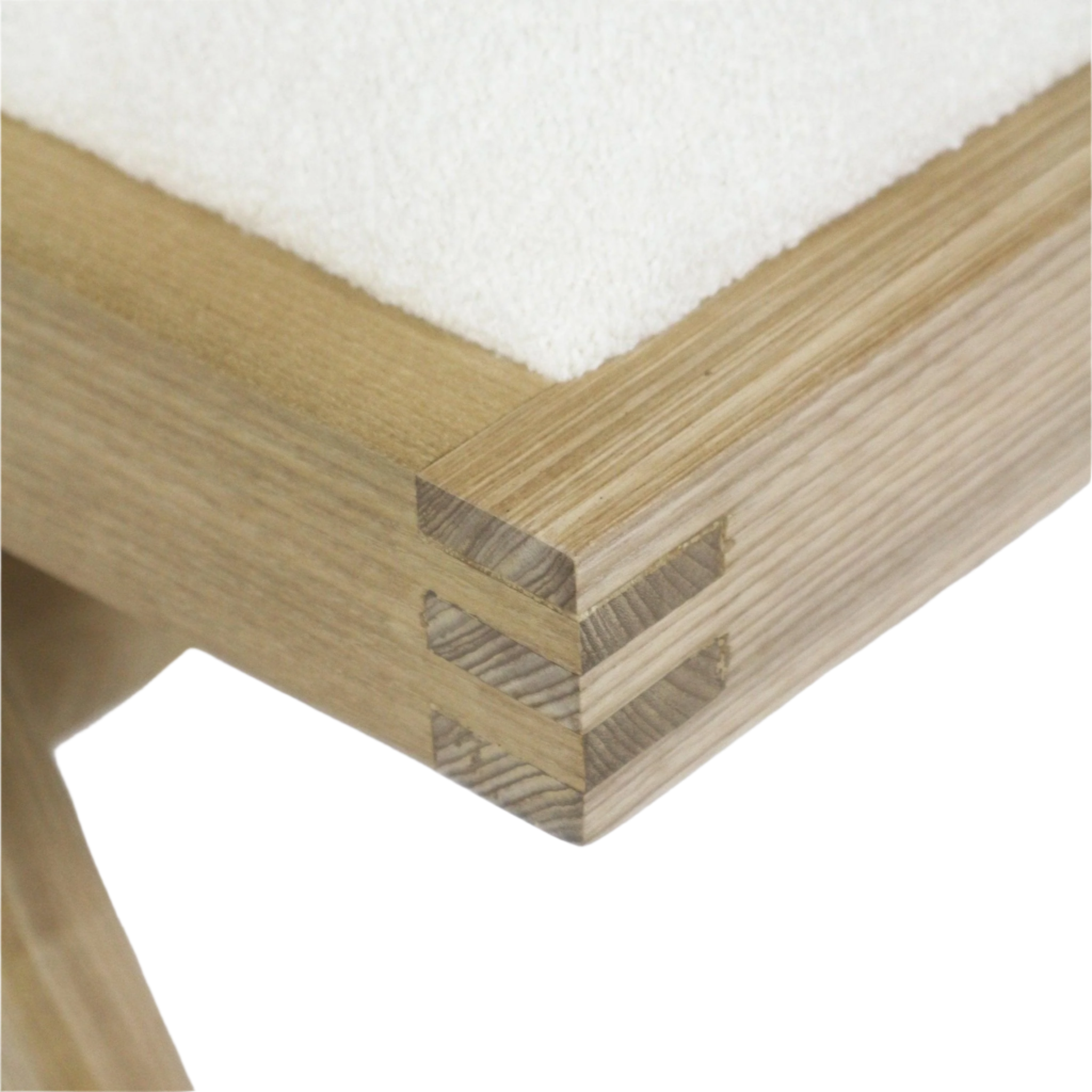 Close-up of a solid ash wood corner with visible finger joints beside a cream boucle upholstered seat top, highlighting light natural wood grain and precise joinery on the armless side chair frame.
