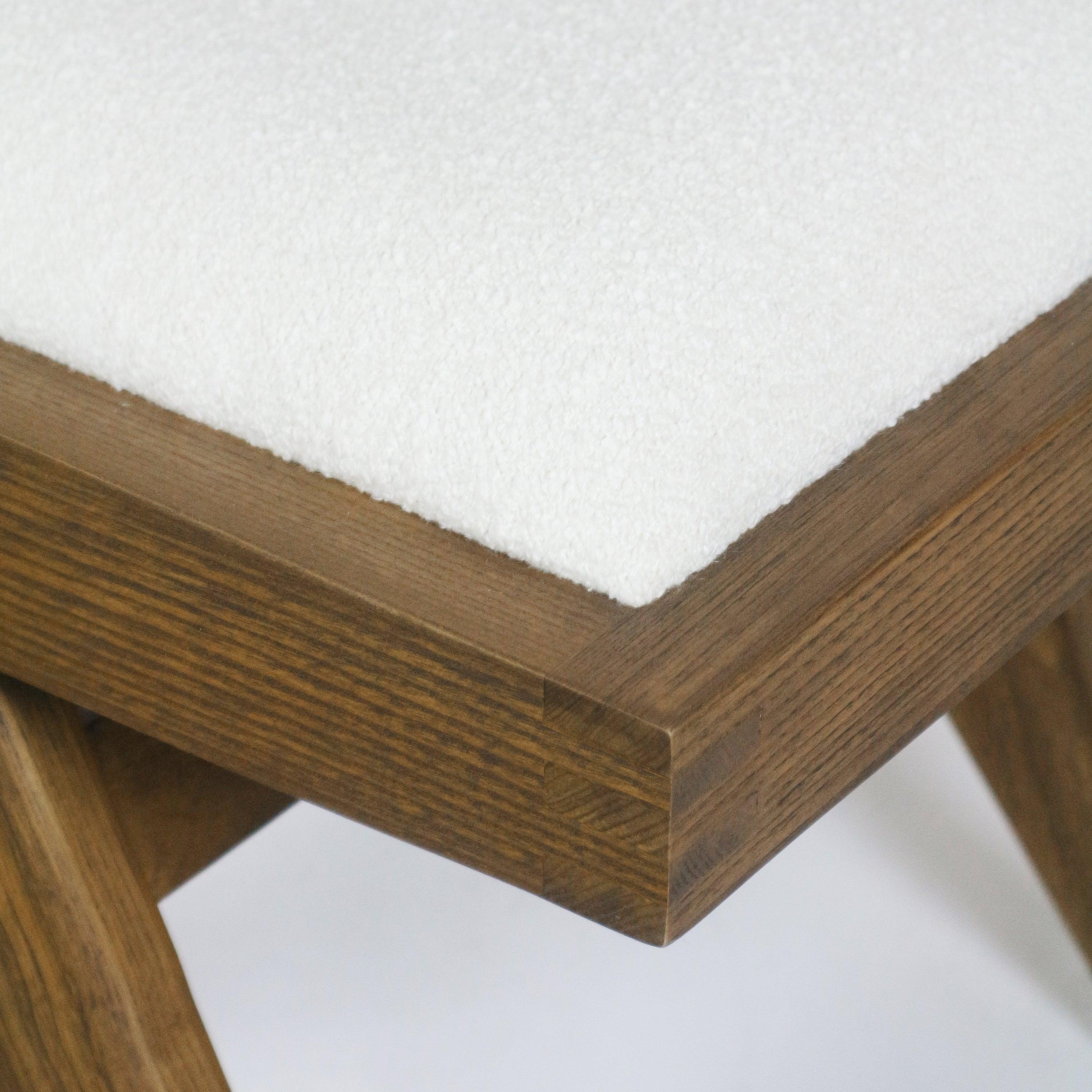 Close-up of the chair seat corner showing cream boucle upholstery on a medium-brown solid ash frame with visible wood grain and mitered joinery detail.