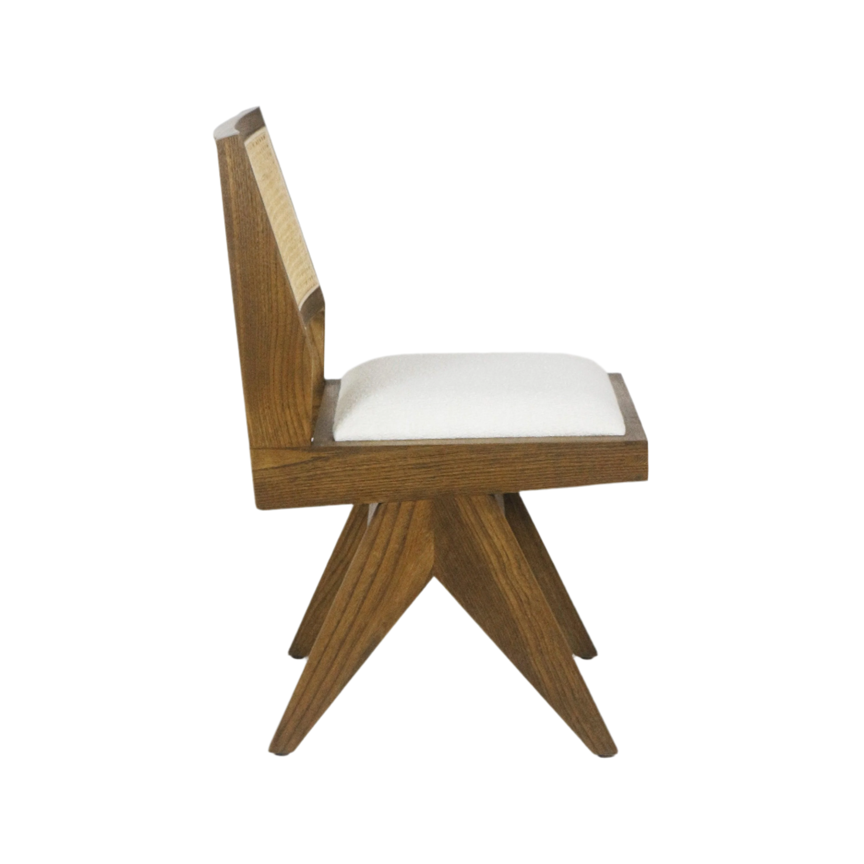 Side view of a mid-century modern armless dining chair with a medium brown solid wood frame, angled star-shaped legs, cane back panel and a cream boucle upholstered seat cushion.