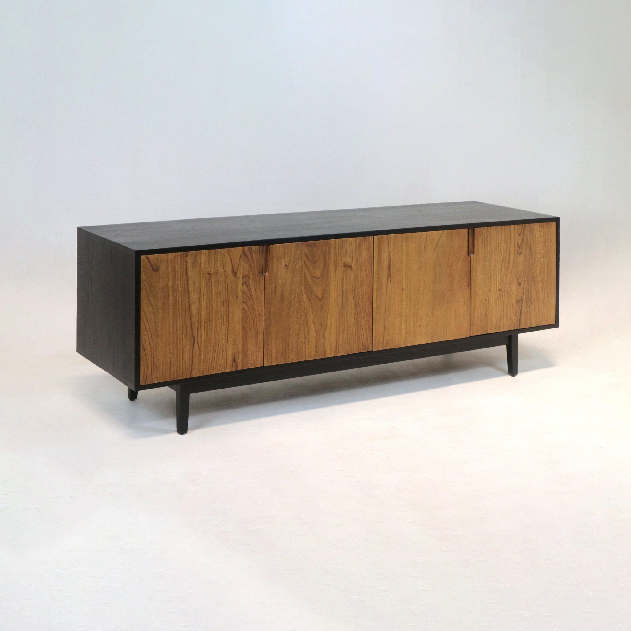 Long mid-century modern teak sideboard with warm teak doors set in a contrasting black solid-wood frame, tapered legs and four recessed-pull cabinet panels, photographed on a pale studio backdrop.