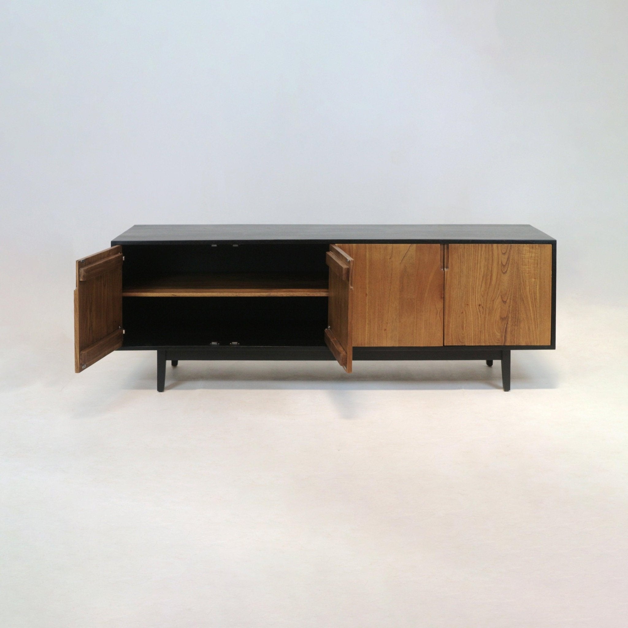 Long mid-century modern teak sideboard with a black frame and tapered legs, three teak doors (two open) revealing an internal shelf, photographed on a light studio background.