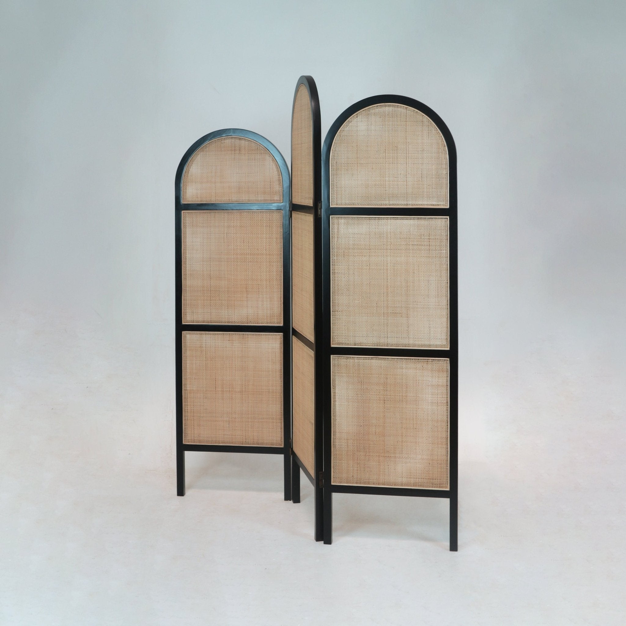Three-panel freestanding room divider with arched tops, black solid wood frames and natural woven rattan cane panels, a boho-style privacy screen for living room or bedroom.