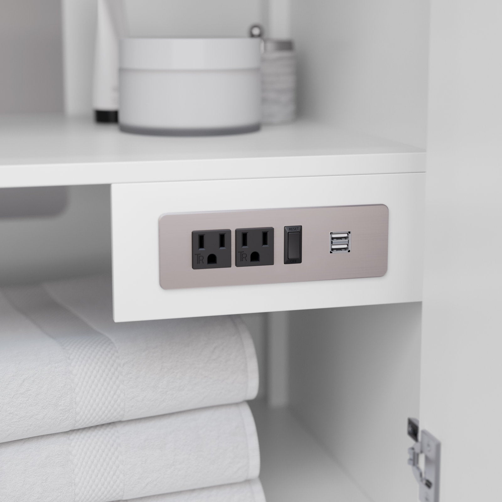 Interior shelf of a white solid-wood bathroom vanity showing a brushed-nickel outlet plate with two black power sockets, a reset switch and dual USB ports above neatly folded white towels.